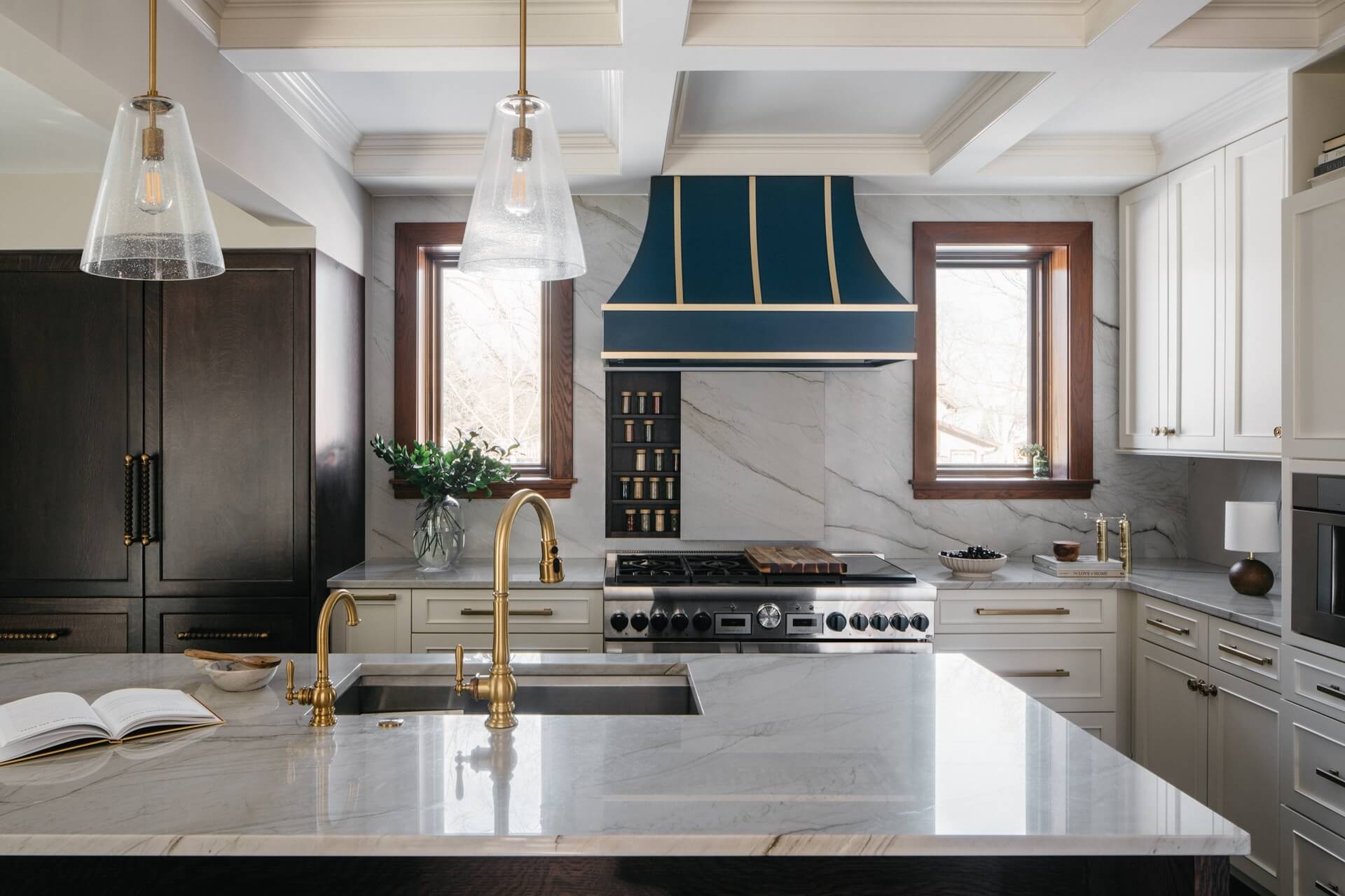 Elegant remodeled kitchen with blue range hood, white cabinetry, brass fixtures, marble backsplash, and expansive island workspace.