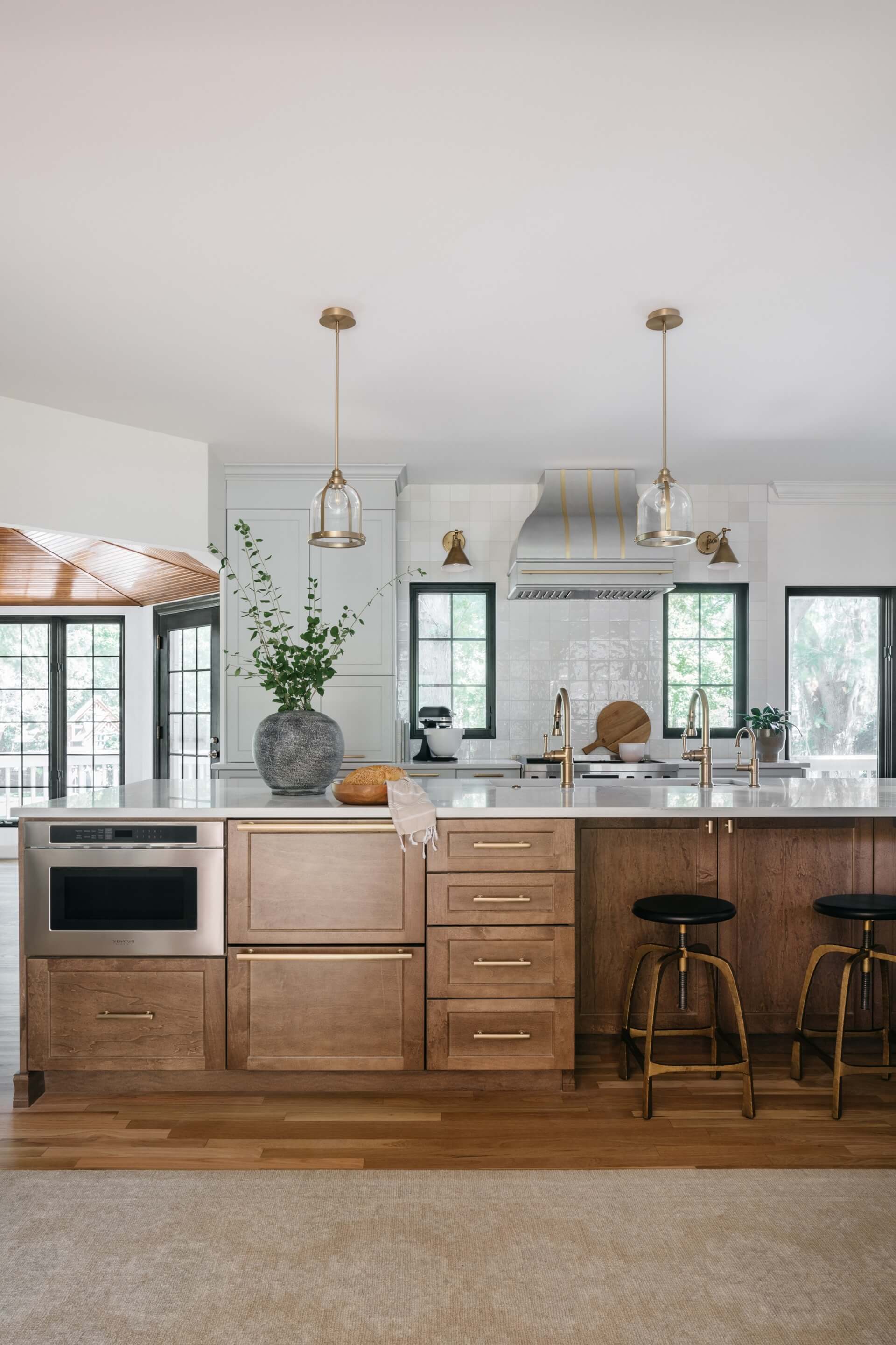 Modern remodeled kitchen features wood cabinetry, marble island, pendant lights, stainless appliances, and bright windows.