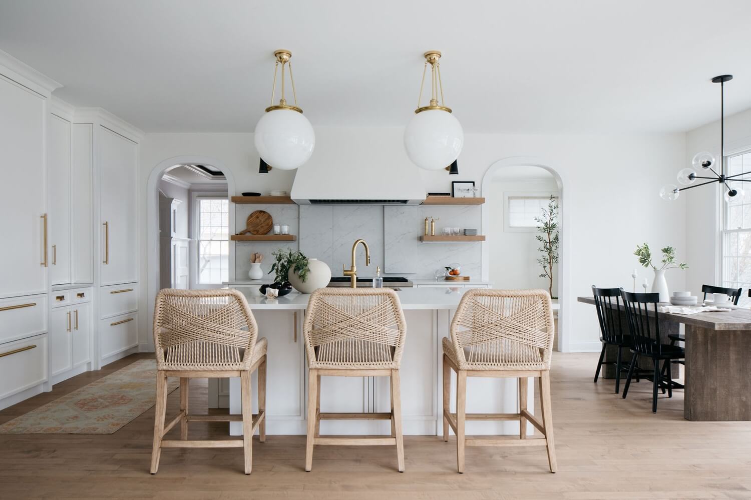 Remodeled kitchen with rattan bar stools, white cabinetry, marble backsplash, pendant lights, and natural wood flooring.