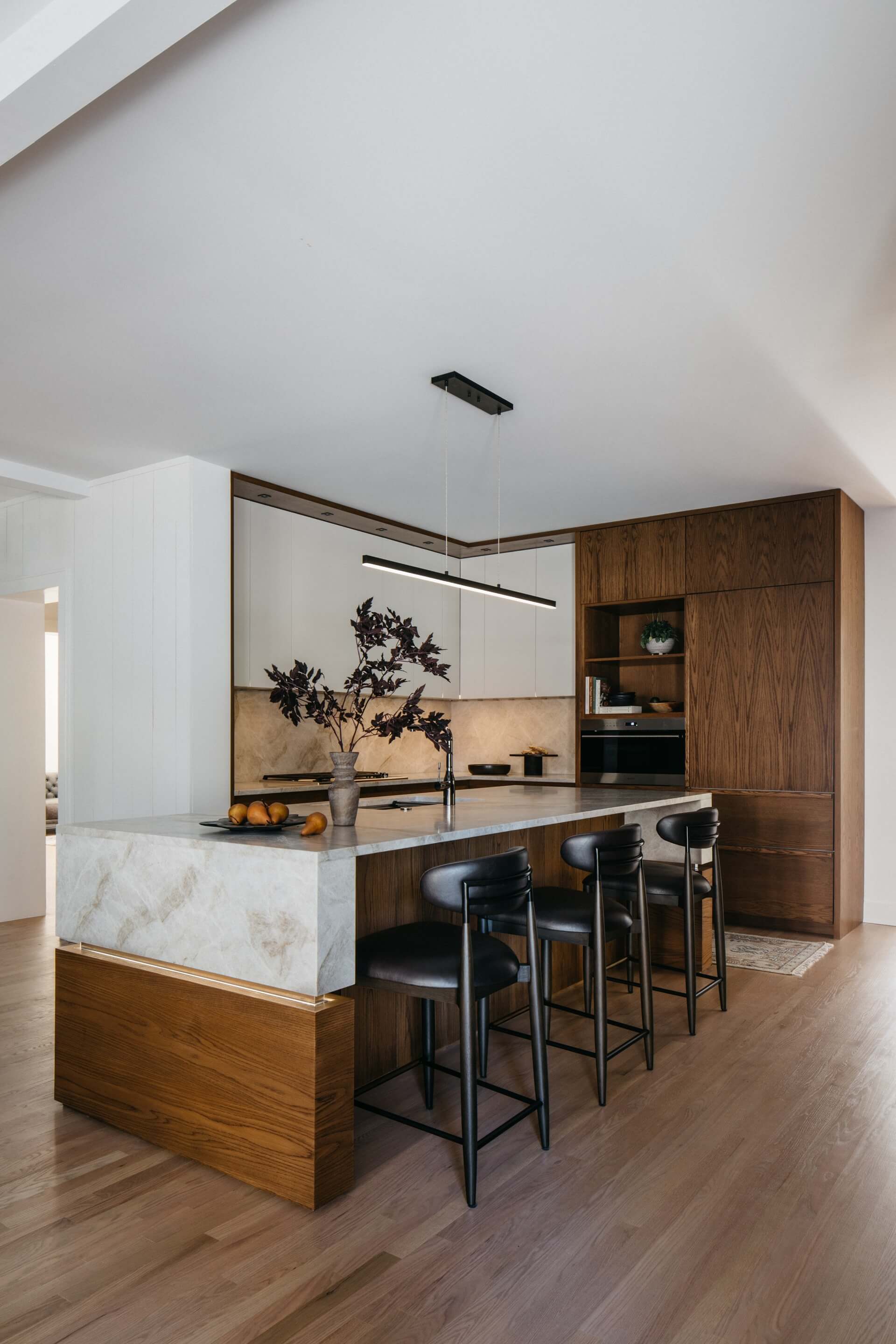 Modern kitchen remodel featuring marble island, dark wood cabinetry, black bar stools, sleek appliances, and warm flooring.