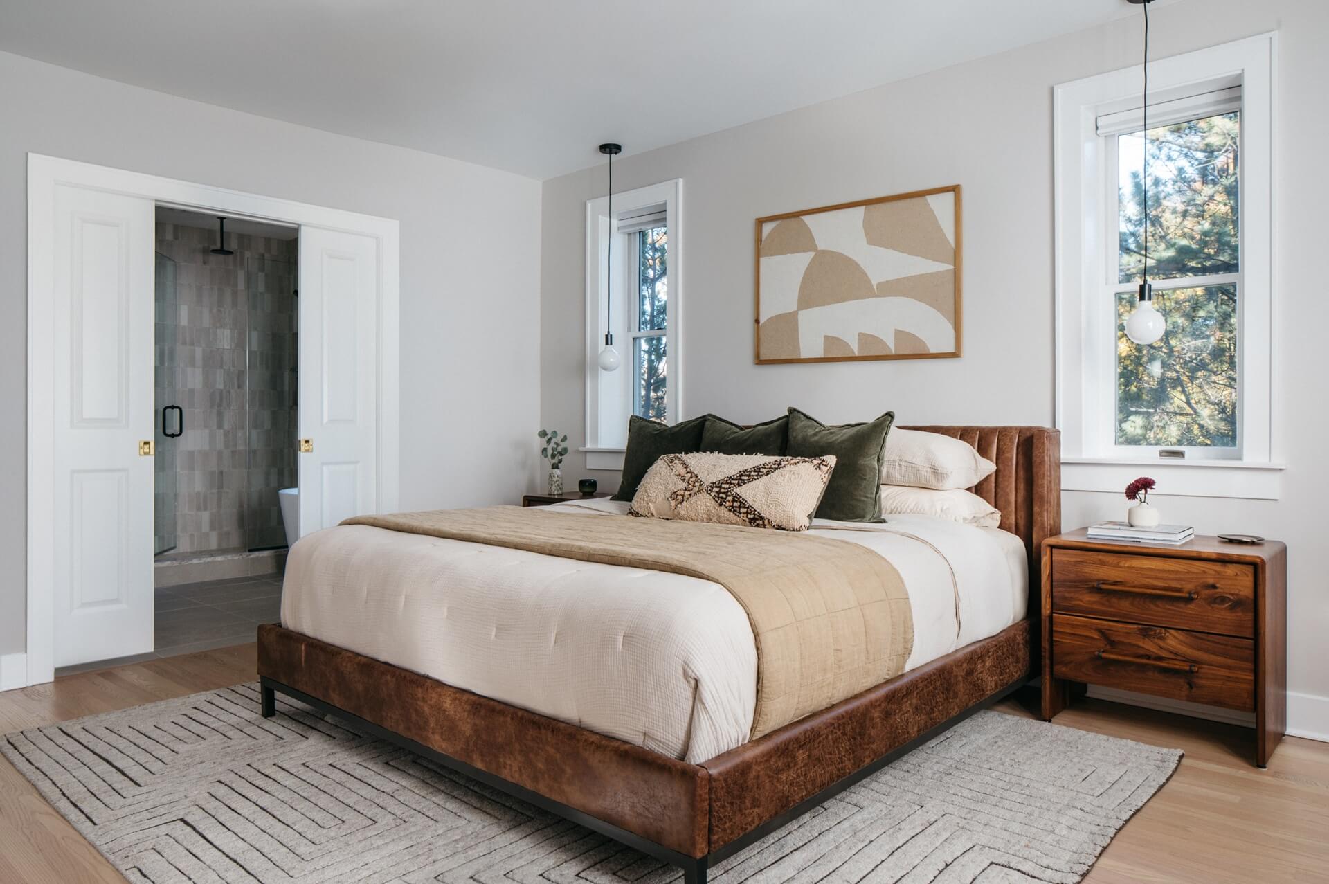 Remodeled bedroom features a wooden bed, neutral bedding, textured rug, artwork, and soft natural lighting.