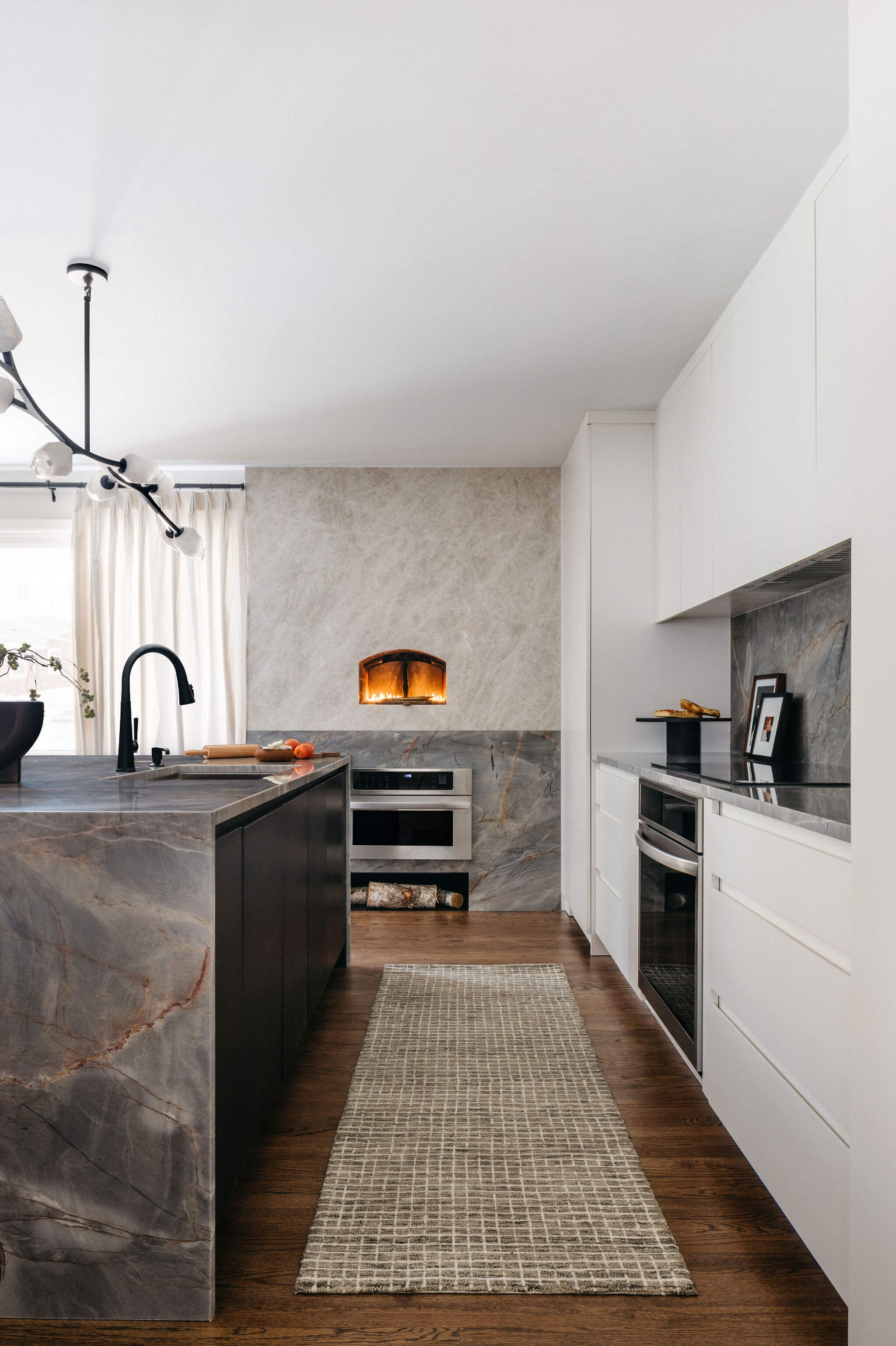 Luxury kitchen remodel with dramatic stone surfaces, dark cabinetry, white storage, integrated appliances, and warm wood flooring.