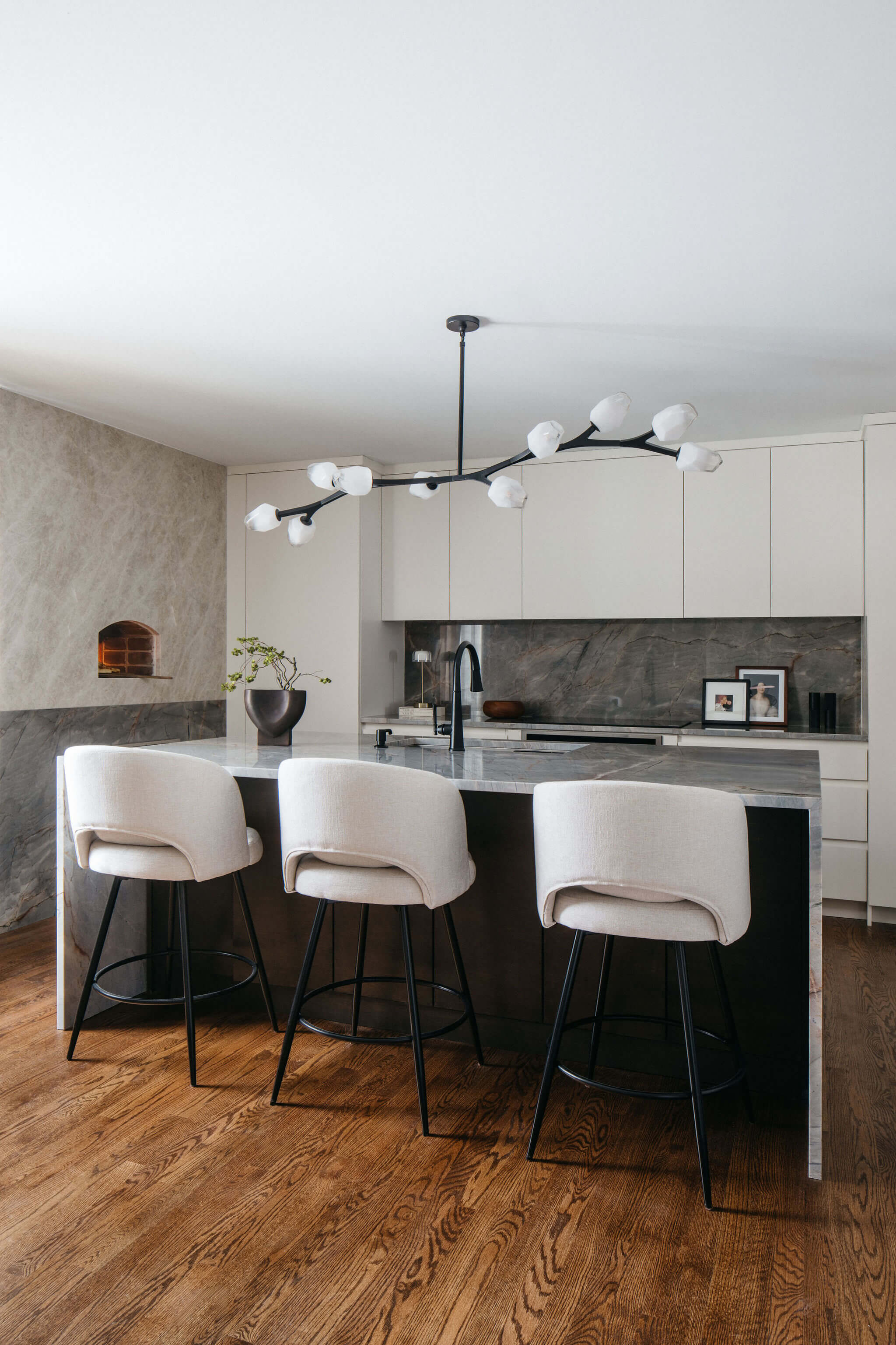 Inviting kitchen remodel with white cabinets, wood island seating, pendant lights, marble counters, and fresh floral accents.