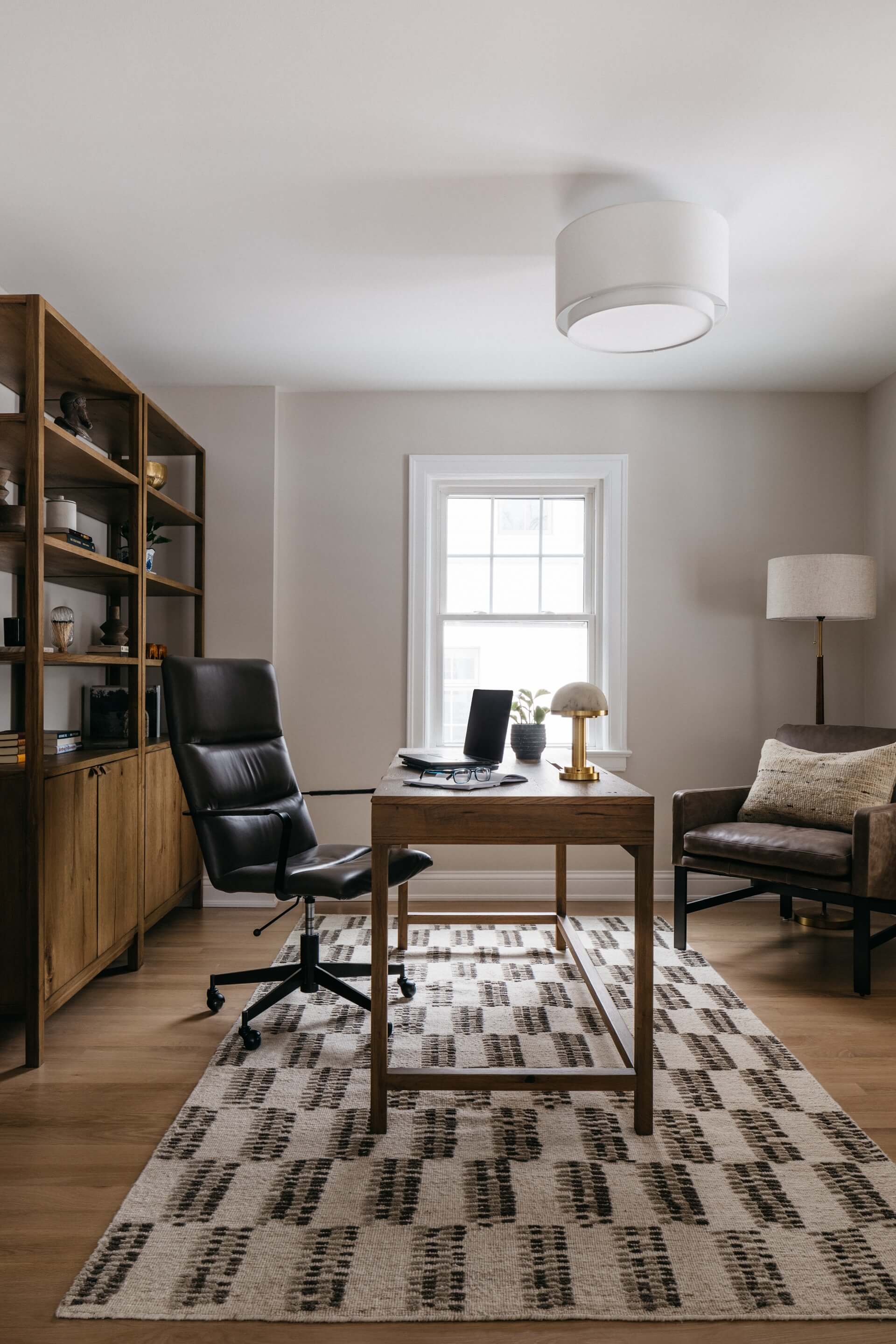 Remodeled home office features built in shelving, leather chair, desk, window, and patterned rug.
