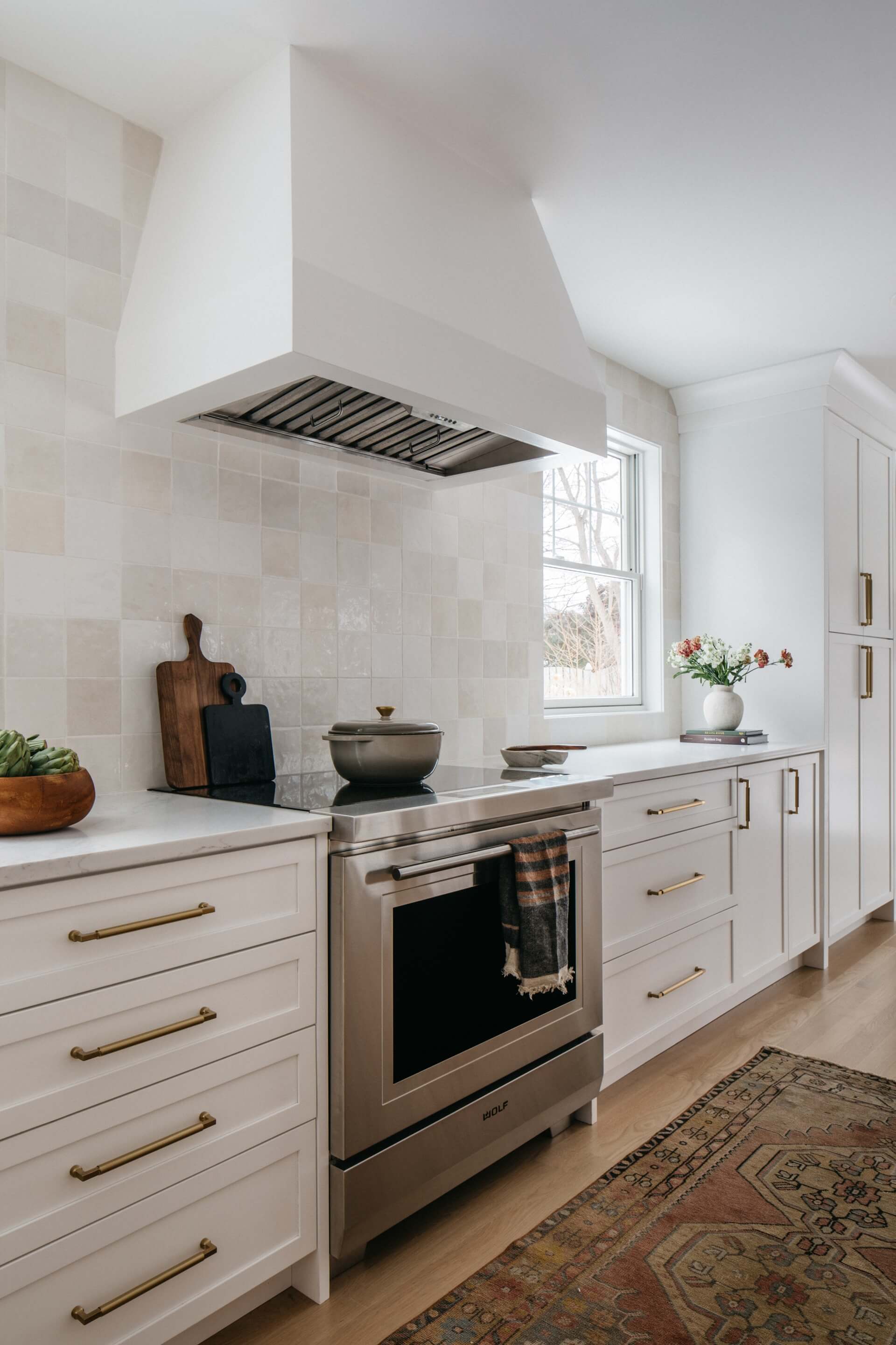 White kitchen remodel with brass hardware, stainless range, subway backsplash, natural light, and patterned area rug.