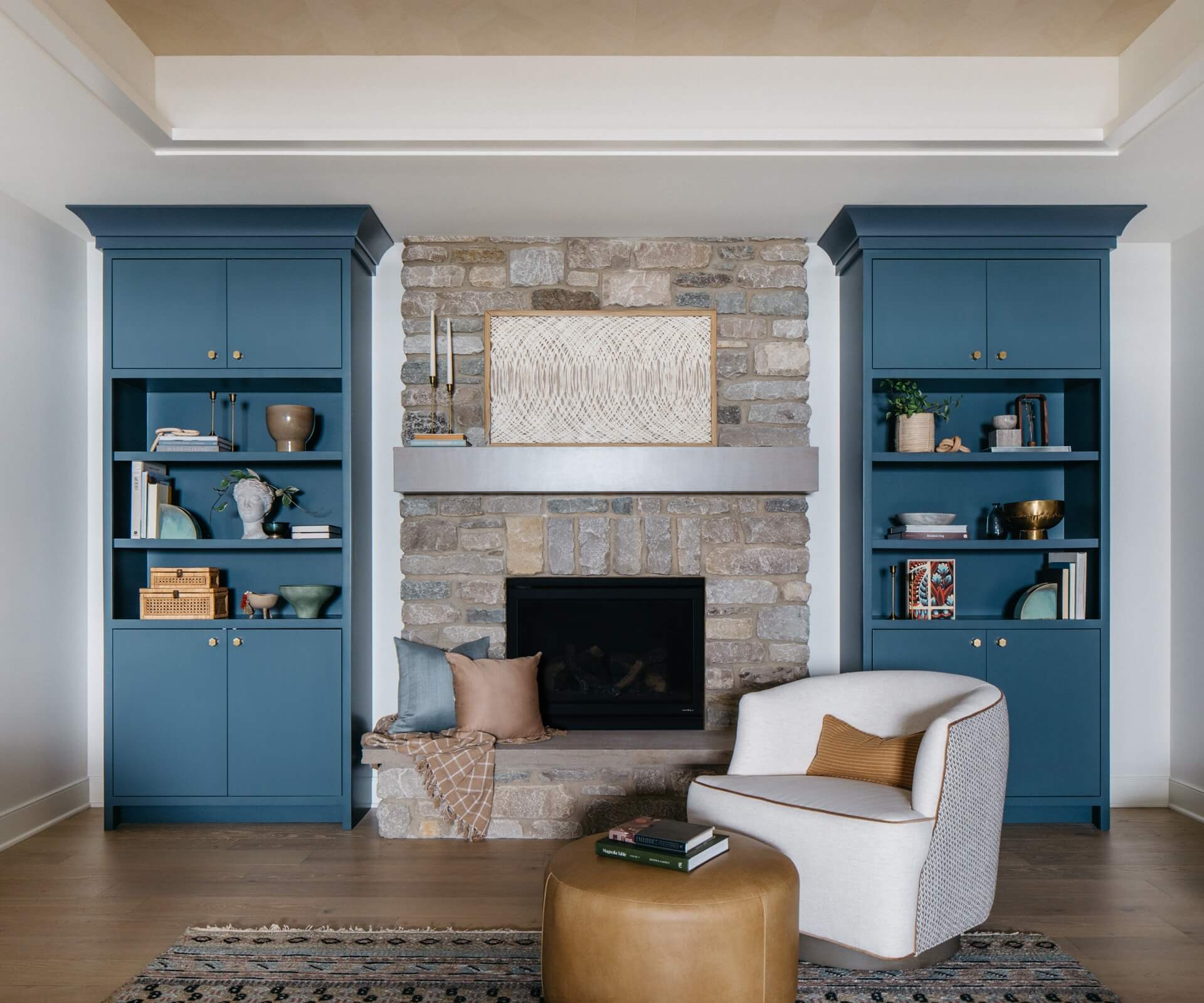 Remodeled living room featuring blue built ins, a stone fireplace, artwork, seating, and warm wood flooring.