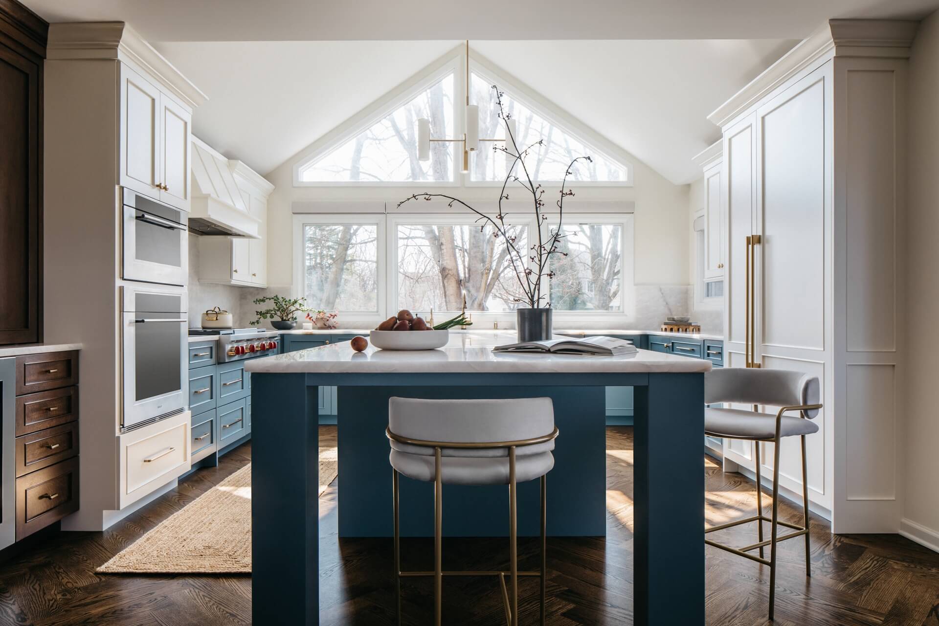 Remodeled kitchen features blue cabinetry, large windows, central island, pendant lights, and contemporary bar seating.