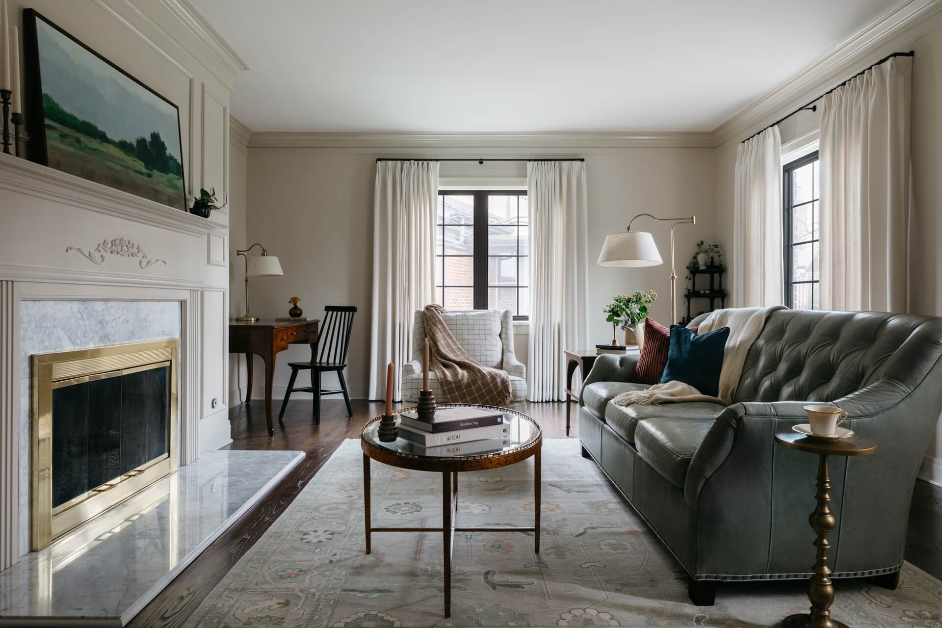 Remodeled living room featuring a marble fireplace, leather sofa, coffee table, armchairs, plants, and layered lighting.