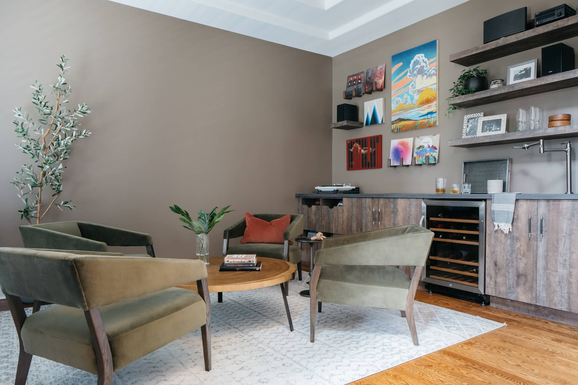 Remodeled living room features colorful artwork, wood cabinetry, modern chairs, coffee table, and neutral patterned flooring.